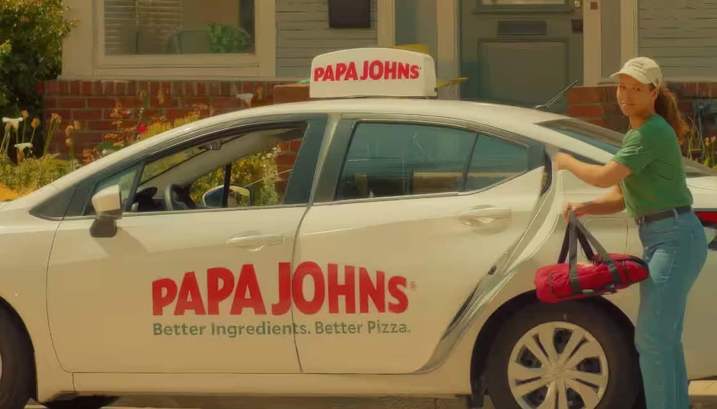 Papa Johns delivery driver loading pizzas into a Papa Johns delivery car